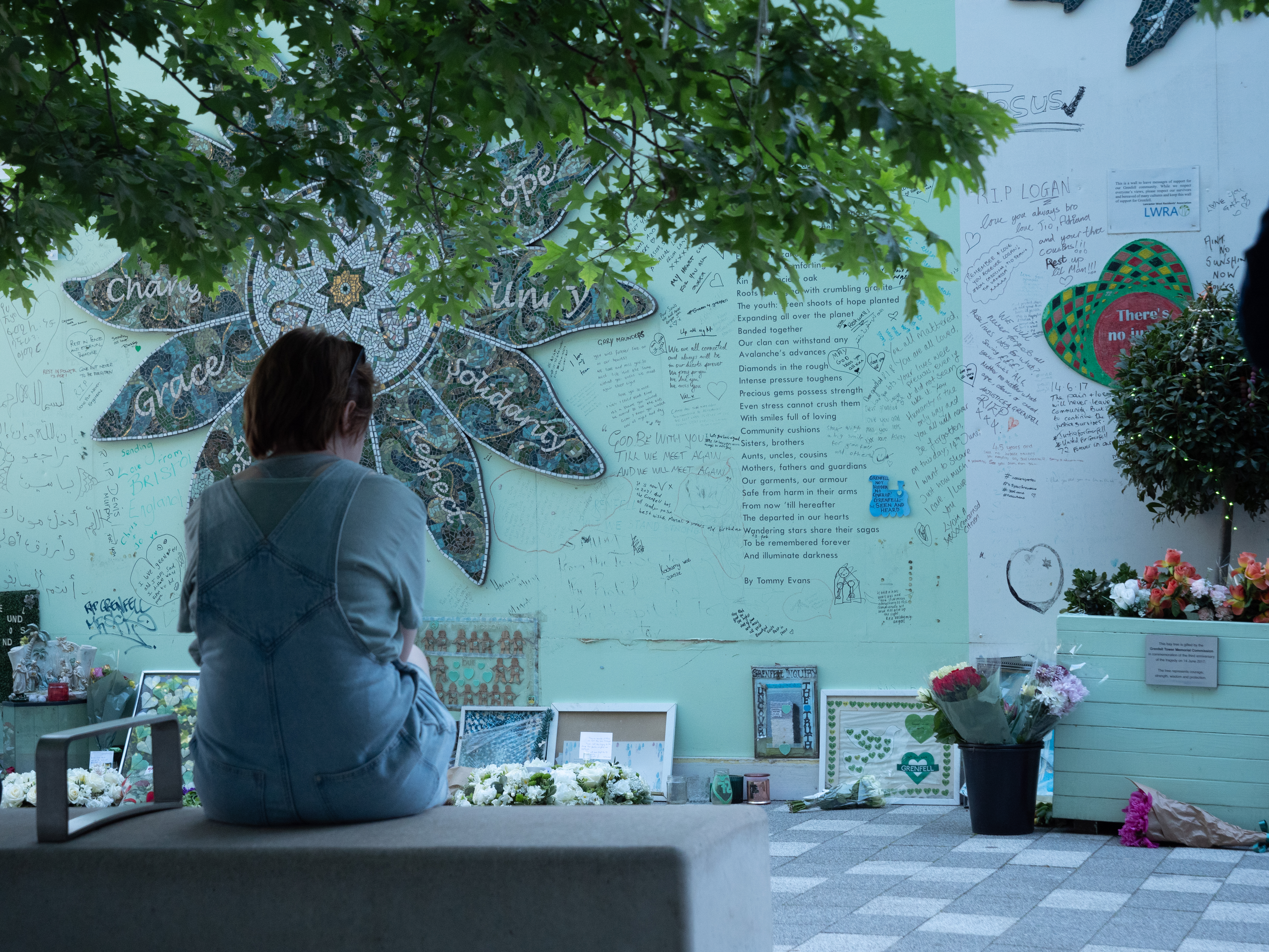 An image of a person sitting and looking at the Grenfell memorial wall.